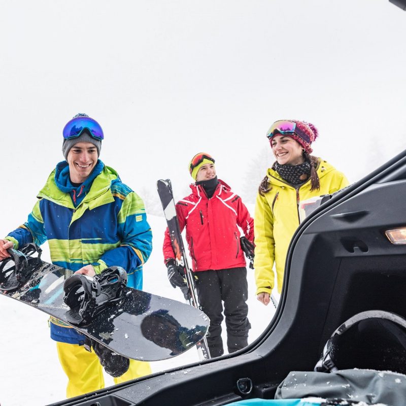 Friends with ski and snow board unloading stuff from the car. Winter sport scene with a group of young people wearing skiing clothes and smiling. Sport and lifestyle concepts
